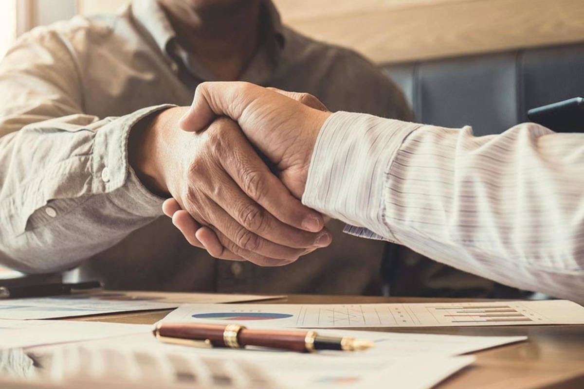 Closeup of two men shaking hand with documents and a pen laying on the table